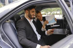 Smiling business analysts have online meeting using laptop while sitting in car back seats photo