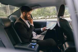 Confidence businessman sitting on car backseat and working with documents while going to office photo