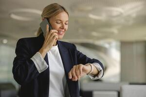 Female sales manager looking at wristwatch to checking time while having a phone call with client photo