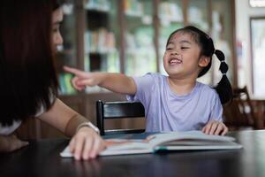 Asian woman is pointing at book with a child. The child is smiling and he is enjoying the activity. The woman is likely teaching the child how to read, helping them with a school assignment photo