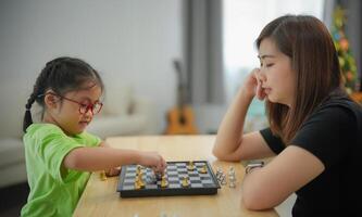 Asian woman and a little girl are playing a game of chess. The woman is looking at the board and the girl is making a move. Scene is calm and focused, as both players are concentrating on the game photo