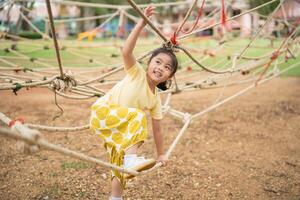 Asian young girl is climbing a rope course in a park. She is smiling and she is enjoying herself photo