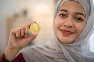 Muslim islam woman with hijab is holding a gold coin with the letter B on it. She is smiling and she is happy photo