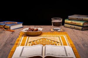 Many Date Palms are on bowls, plates, and cups of water, and the Quran is on wooden tables, to wait for the time of Iftar, with the concept of ramadan Muslims, Arabic calligraphy meaning of Al Quran photo