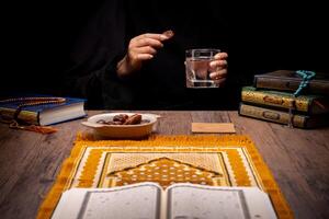 Many Date Palms are on bowls, plates, and cups of water, and the Quran is on wooden tables, to wait for the time of Iftar, with the concept of ramadan Muslims, Arabic calligraphy meaning of Al Quran photo
