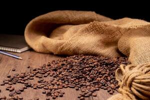 The picture of coffee beans stacked together on a wooden floor in a warm, light atmosphere, on a dark background, with copy space. photo