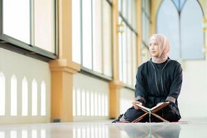 The image of an Asian Muslim woman in the Islamic religion in hijab in cream color. reading the Quran and having a happy smiling face Staying in a beautiful mosque out of respect for God. photo