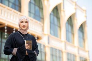 The image of an Asian Muslim woman in the Islamic religion in hijab in cream color. reading the Quran and having a happy smiling face Staying in a beautiful mosque out of respect for God. photo