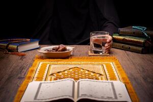 Many Date Palms are on bowls, plates, and cups of water, and the Quran is on wooden tables, to wait for the time of Iftar, with the concept of ramadan Muslims, Arabic calligraphy meaning of Al Quran photo
