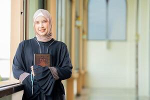 The image of an Asian Muslim woman in the Islamic religion in hijab in cream color. reading the Quran and having a happy smiling face Staying in a beautiful mosque out of respect for God. photo