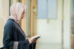 The image of an Asian Muslim woman in the Islamic religion in hijab in cream color. reading the Quran and having a happy smiling face Staying in a beautiful mosque out of respect for God. photo