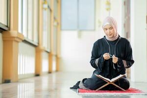 The image of an Asian Muslim woman in the Islamic religion in hijab in cream color. reading the Quran and having a happy smiling face Staying in a beautiful mosque out of respect for God. photo