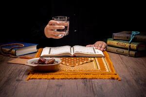 Many Date Palms are on bowls, plates, and cups of water, and the Quran is on wooden tables, to wait for the time of Iftar, with the concept of ramadan Muslims, Arabic calligraphy meaning of Al Quran photo