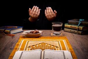 Many Date Palms are on bowls, plates, and cups of water, and the Quran is on wooden tables, to wait for the time of Iftar, with the concept of ramadan Muslims, Arabic calligraphy meaning of Al Quran photo