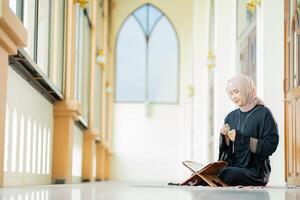 The image of an Asian Muslim woman in the Islamic religion in hijab in cream color. reading the Quran and having a happy smiling face Staying in a beautiful mosque out of respect for God. photo
