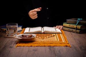 Many Date Palms are on bowls, plates, and cups of water, and the Quran is on wooden tables, to wait for the time of Iftar, with the concept of ramadan Muslims, Arabic calligraphy meaning of Al Quran photo