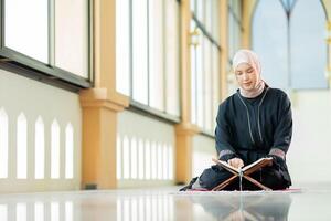 The image of an Asian Muslim woman in the Islamic religion in hijab in cream color. reading the Quran and having a happy smiling face Staying in a beautiful mosque out of respect for God. photo