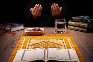 Many Date Palms are on bowls, plates, and cups of water, and the Quran is on wooden tables, to wait for the time of Iftar, with the concept of ramadan Muslims, Arabic calligraphy meaning of Al Quran photo