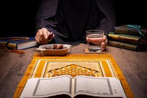 Many Date Palms are on bowls, plates, and cups of water, and the Quran is on wooden tables, to wait for the time of Iftar, with the concept of ramadan Muslims, Arabic calligraphy meaning of Al Quran photo