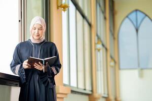 The image of an Asian Muslim woman in the Islamic religion in hijab in cream color. reading the Quran and having a happy smiling face Staying in a beautiful mosque out of respect for God. photo