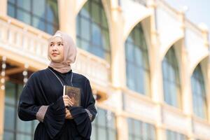 The image of an Asian Muslim woman in the Islamic religion in hijab in cream color. reading the Quran and having a happy smiling face Staying in a beautiful mosque out of respect for God. photo