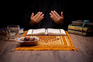 Many Date Palms are on bowls, plates, and cups of water, and the Quran is on wooden tables, to wait for the time of Iftar, with the concept of ramadan Muslims, Arabic calligraphy meaning of Al Quran photo