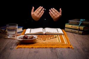 Many Date Palms are on bowls, plates, and cups of water, and the Quran is on wooden tables, to wait for the time of Iftar, with the concept of ramadan Muslims, Arabic calligraphy meaning of Al Quran photo