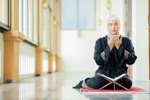 The image of an Asian Muslim woman in the Islamic religion in hijab in cream color. reading the Quran and having a happy smiling face Staying in a beautiful mosque out of respect for God. photo