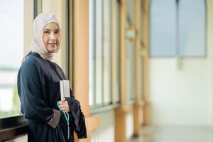 The image of an Asian Muslim woman in the Islamic religion in hijab in cream color. reading the Quran and having a happy smiling face Staying in a beautiful mosque out of respect for God. photo