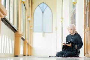 The image of an Asian Muslim woman in the Islamic religion in hijab in cream color. reading the Quran and having a happy smiling face Staying in a beautiful mosque out of respect for God. photo