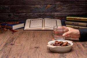 Many Date Palms are on bowls, plates, and cups of water, and the Quran is on wooden tables, to wait for the time of Iftar, with the concept of ramadan Muslims, Arabic calligraphy meaning of Al Quran photo