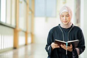 The image of an Asian Muslim woman in the Islamic religion in hijab in cream color. reading the Quran and having a happy smiling face Staying in a beautiful mosque out of respect for God. photo