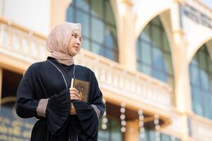The image of an Asian Muslim woman in the Islamic religion in hijab in cream color. reading the Quran and having a happy smiling face Staying in a beautiful mosque out of respect for God. photo