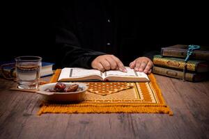 Many Date Palms are on bowls, plates, and cups of water, and the Quran is on wooden tables, to wait for the time of Iftar, with the concept of ramadan Muslims, Arabic calligraphy meaning of Al Quran photo