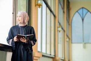 The image of an Asian Muslim woman in the Islamic religion in hijab in cream color. reading the Quran and having a happy smiling face Staying in a beautiful mosque out of respect for God. photo
