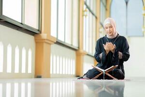 The image of an Asian Muslim woman in the Islamic religion in hijab in cream color. reading the Quran and having a happy smiling face Staying in a beautiful mosque out of respect for God. photo
