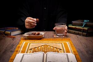Many Date Palms are on bowls, plates, and cups of water, and the Quran is on wooden tables, to wait for the time of Iftar, with the concept of ramadan Muslims, Arabic calligraphy meaning of Al Quran photo
