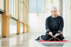 The image of an Asian Muslim woman in the Islamic religion in hijab in cream color. reading the Quran and having a happy smiling face Staying in a beautiful mosque out of respect for God. photo