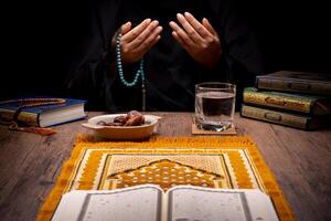 Many Date Palms are on bowls, plates, and cups of water, and the Quran is on wooden tables, to wait for the time of Iftar, with the concept of ramadan Muslims, Arabic calligraphy meaning of Al Quran photo