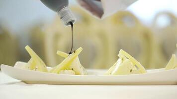 A chef adds delicious sauce to triangular pieces of hard cheese with feta inside on a white plate at a festive table in the restaurant for guests. Close-up. video