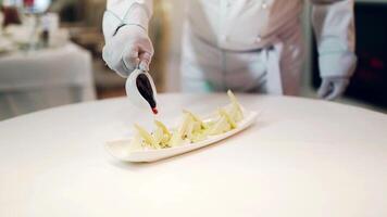 Delicious appetizer of different kinds of cheese is poured by specific red sauce on a white plate. Cook male pours some sauce on pieces of cheese. video