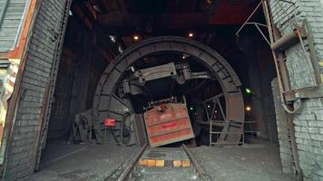 Device for unloading coal from wagon with a deaf body is rotating in the room of factory. Wagon tipper. Camera motion to back. Close-up. video