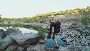 A tourist in summer clothes walks on the edge of a quarry with huge stones and looks at the beautiful lake and the nature around it. Beautiful view. video