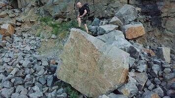 A man in a black t-shirt and a backpack comes to the edge of a large stone and raises his hands up. Tourist got to the center of stone quarry. video
