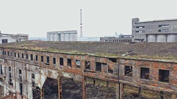 An old abandoned factory hangar with damaged walls on the background of other old structures in the same area. Aerial view. video