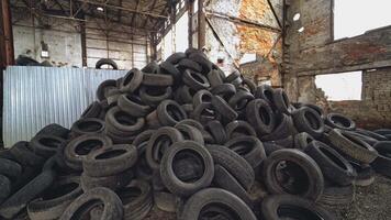Landfill of used automobile tires on the old abandoned plant inside. Huge piles of black waste wheels from different vehicles. Motion bottom up video