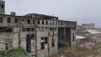 Old abandoned plant with broken windows ruined after the military actions. Demolished plant with pitted roof and some snow on the ground in winter. Aerial view video