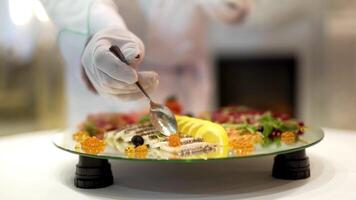 professionnel cuisinier est en mettant caviar par une cuillère sur le assiette avec certains fruit et collations de Viande. chef cuisinier prépare nourriture sur une table dans restaurant, délicieux nourriture est préparé pour visiteurs video