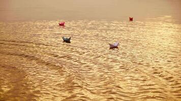 Multy-colored paper boats floating on waves in a river at the evening sunset. Small ships made from paper sail in water. video