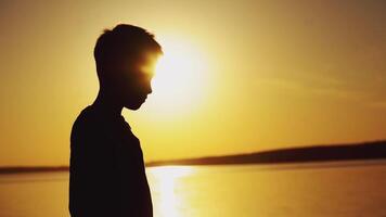 Silhouette of a boy standing near the river and playing with origami ship at a beautiful sunset. Paper boat is in the hands of a little child and bright evening sun video